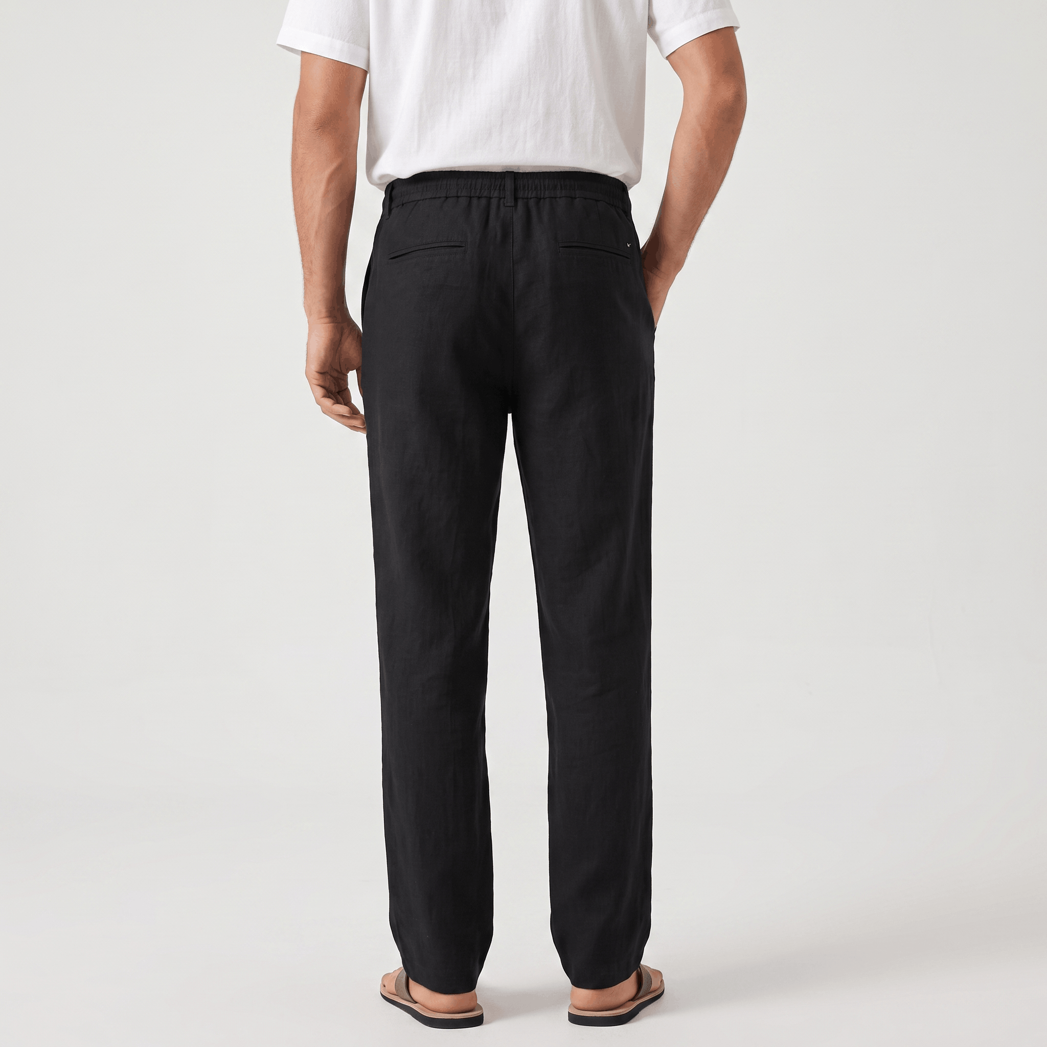 Back view of men's black linen drawstring pants featuring an elastic waistband and relaxed fit.
