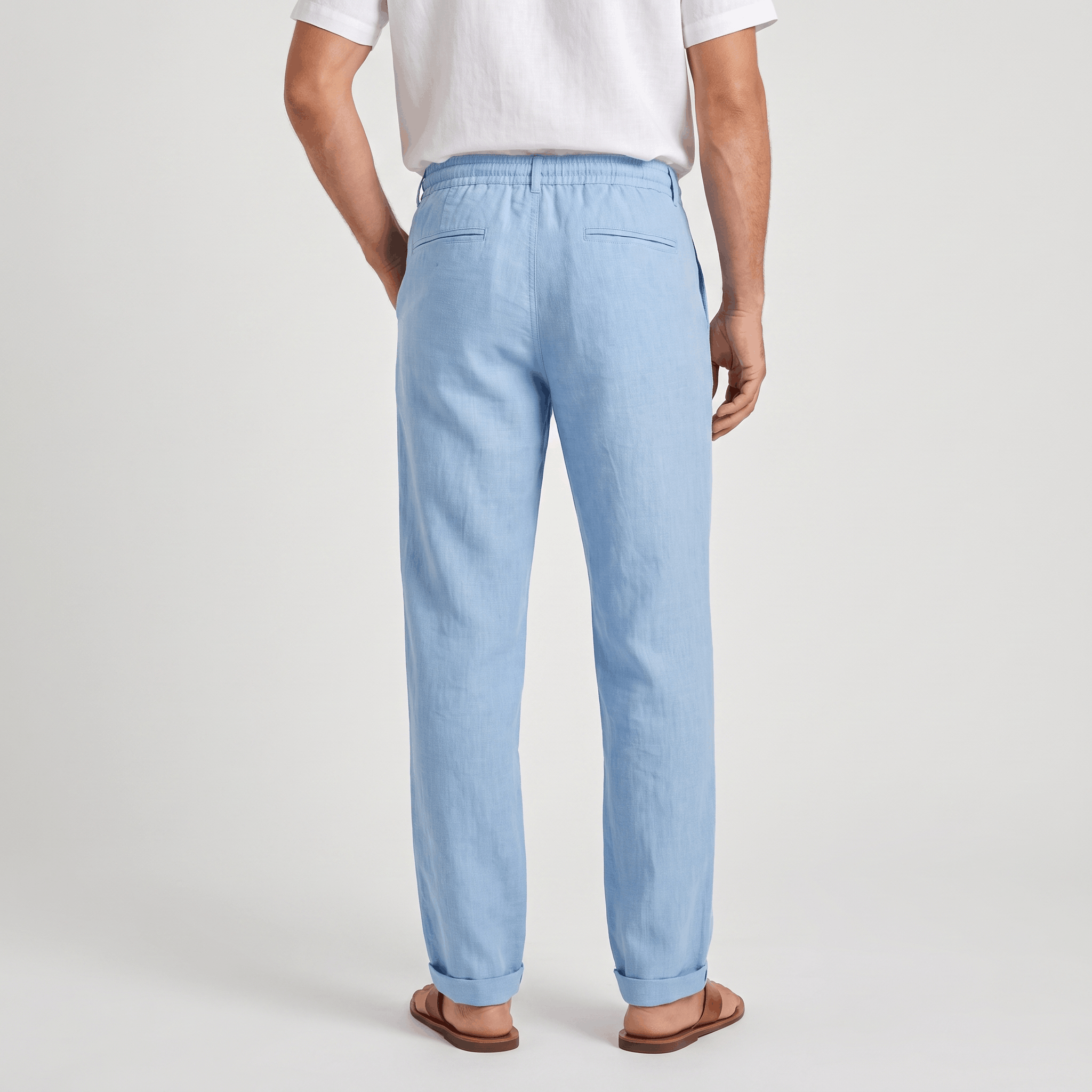 Back view of men's light blue linen drawstring pants with a relaxed silhouette and elastic waistband.