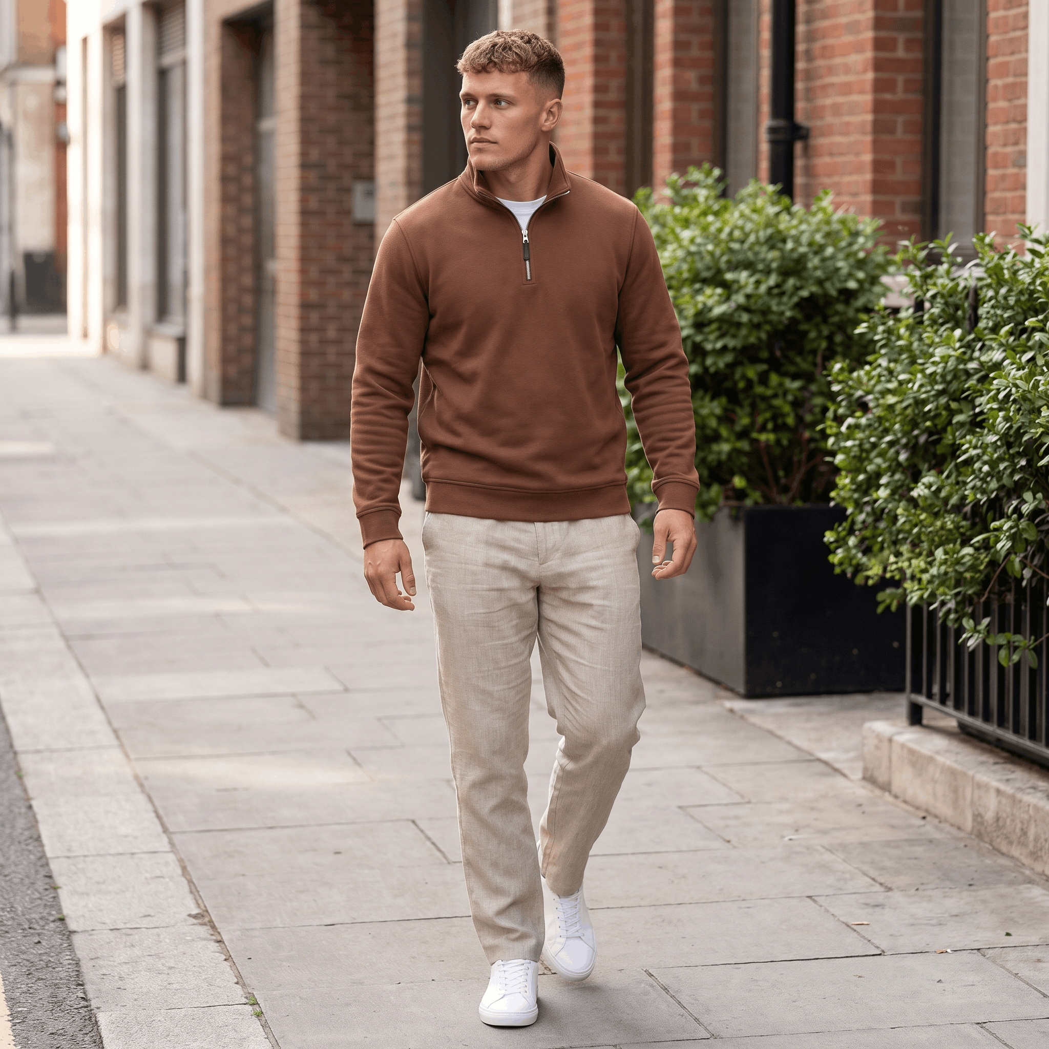 Man wearing a brown quarter-zip knit sweater paired with beige trousers in an urban outdoor setting.