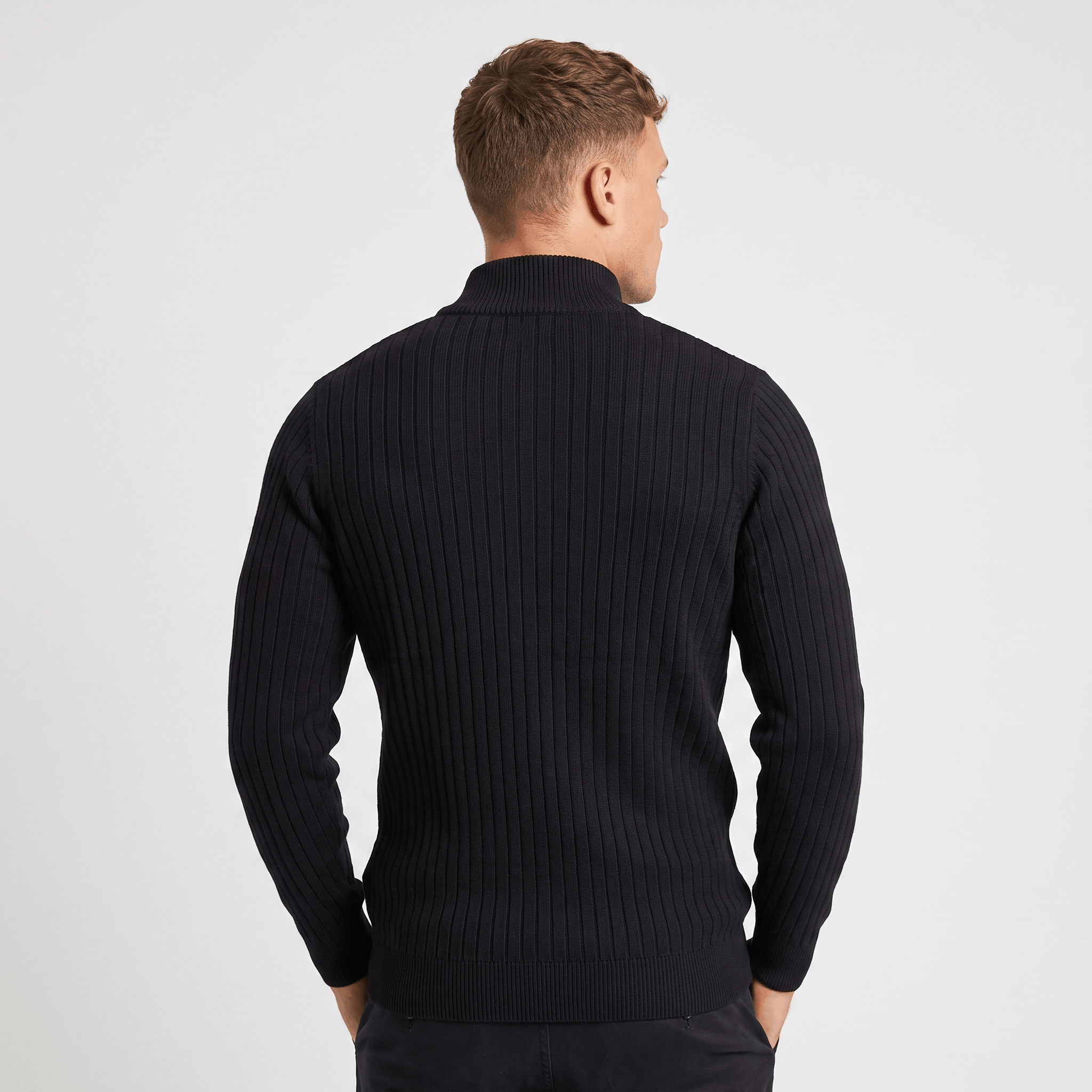 Man wearing a blue ribbed quarter-zip knit sweater with light-colored trousers walking in an urban street setting.