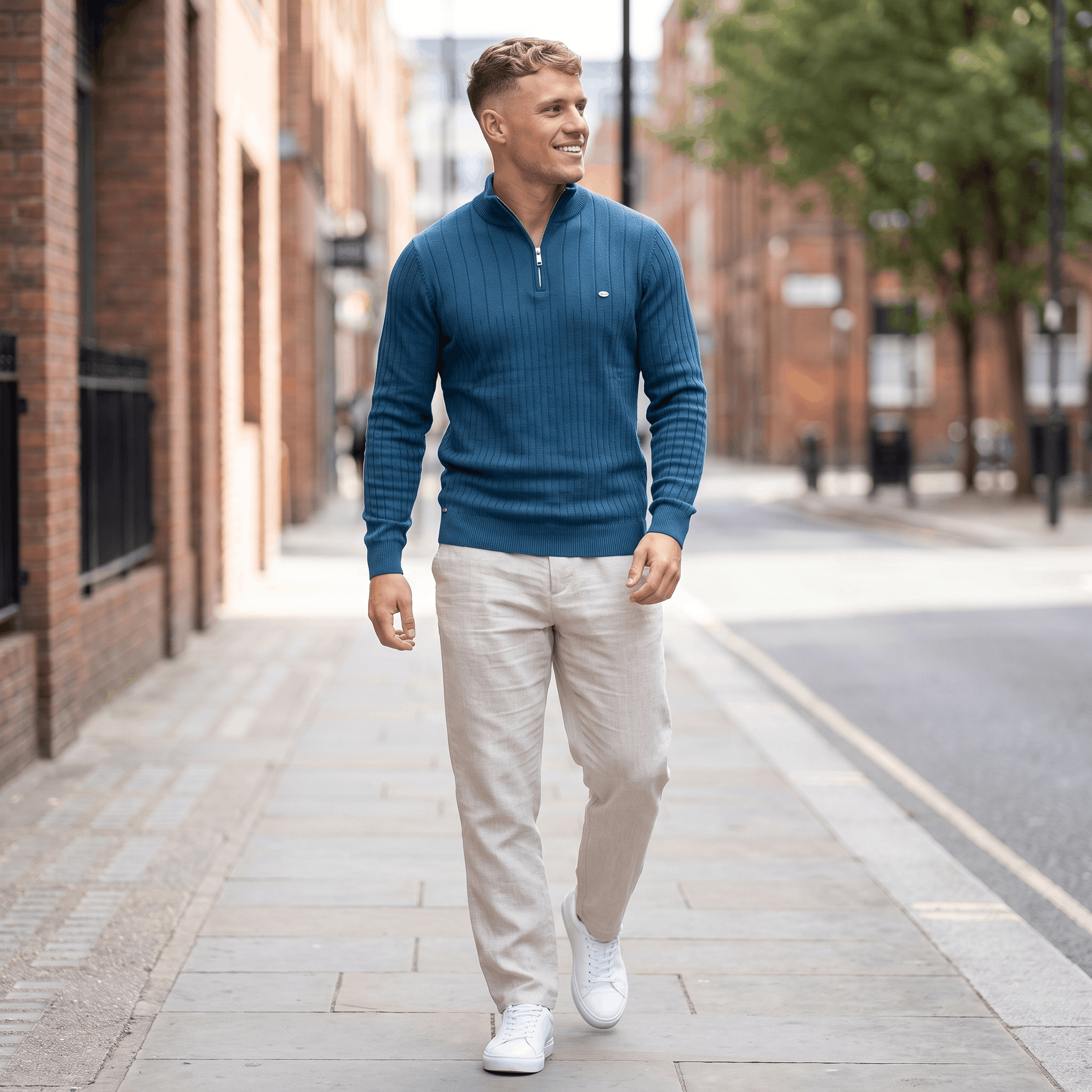Man wearing a blue ribbed quarter-zip knit sweater with light-colored trousers walking in an urban street setting.