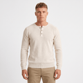 Man wearing a cream waffle knit Henley sweater with a three-button placket, ribbed cuffs, long sleeves, and a classic fit.