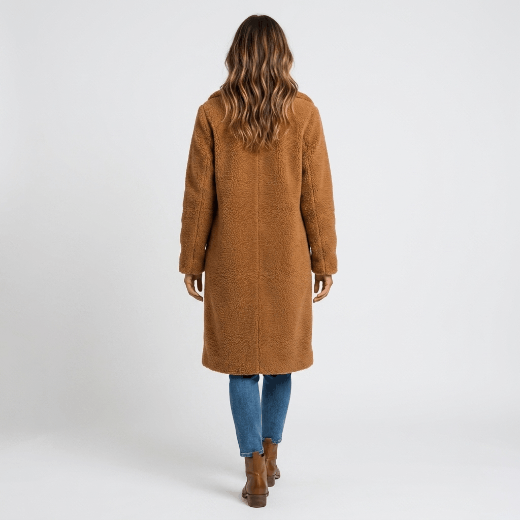 Back view of a woman wearing a camel brown long coat with a structured silhouette, paired with blue jeans and brown ankle boots.