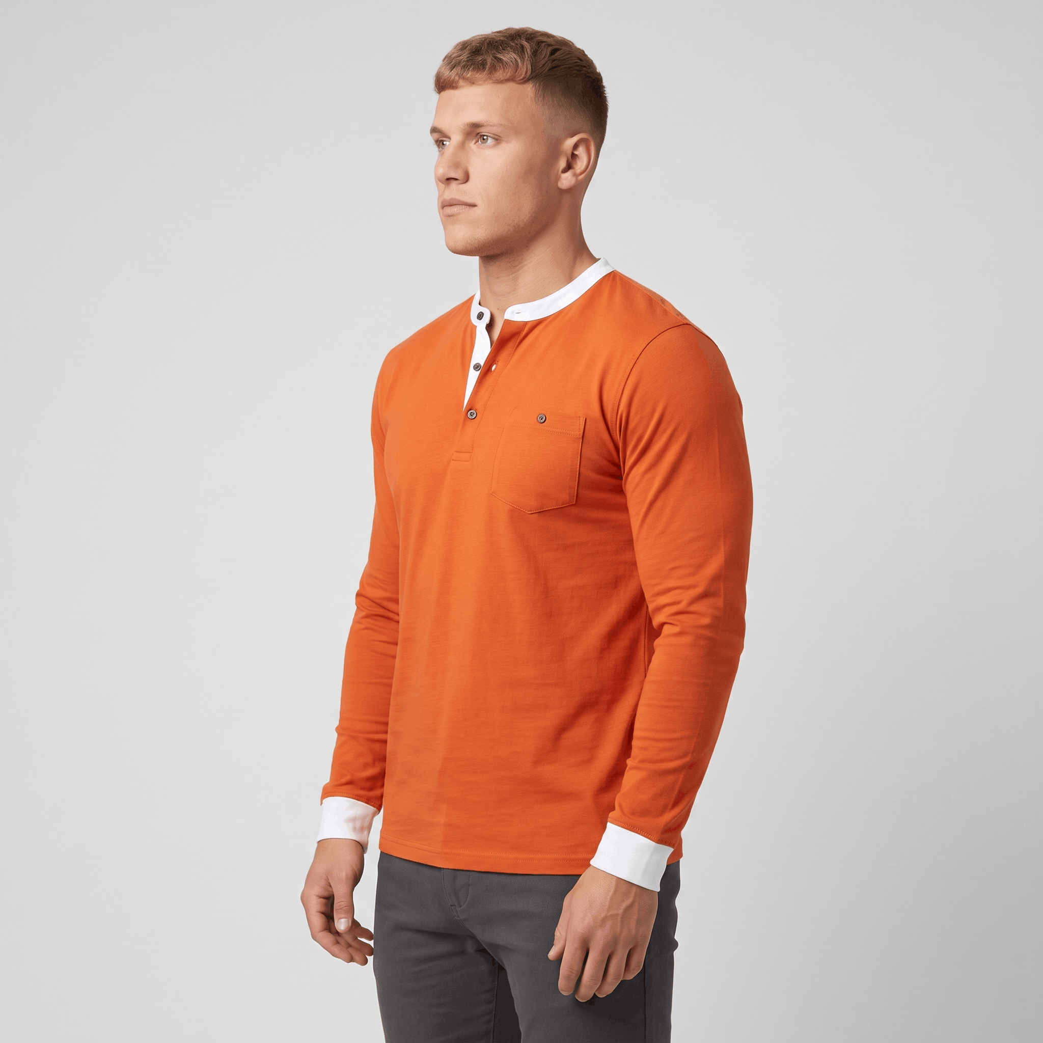 Side view of a man wearing an orange long-sleeve Henley sweater featuring a white contrast placket, ribbed cuffs, and tailored silhouette.