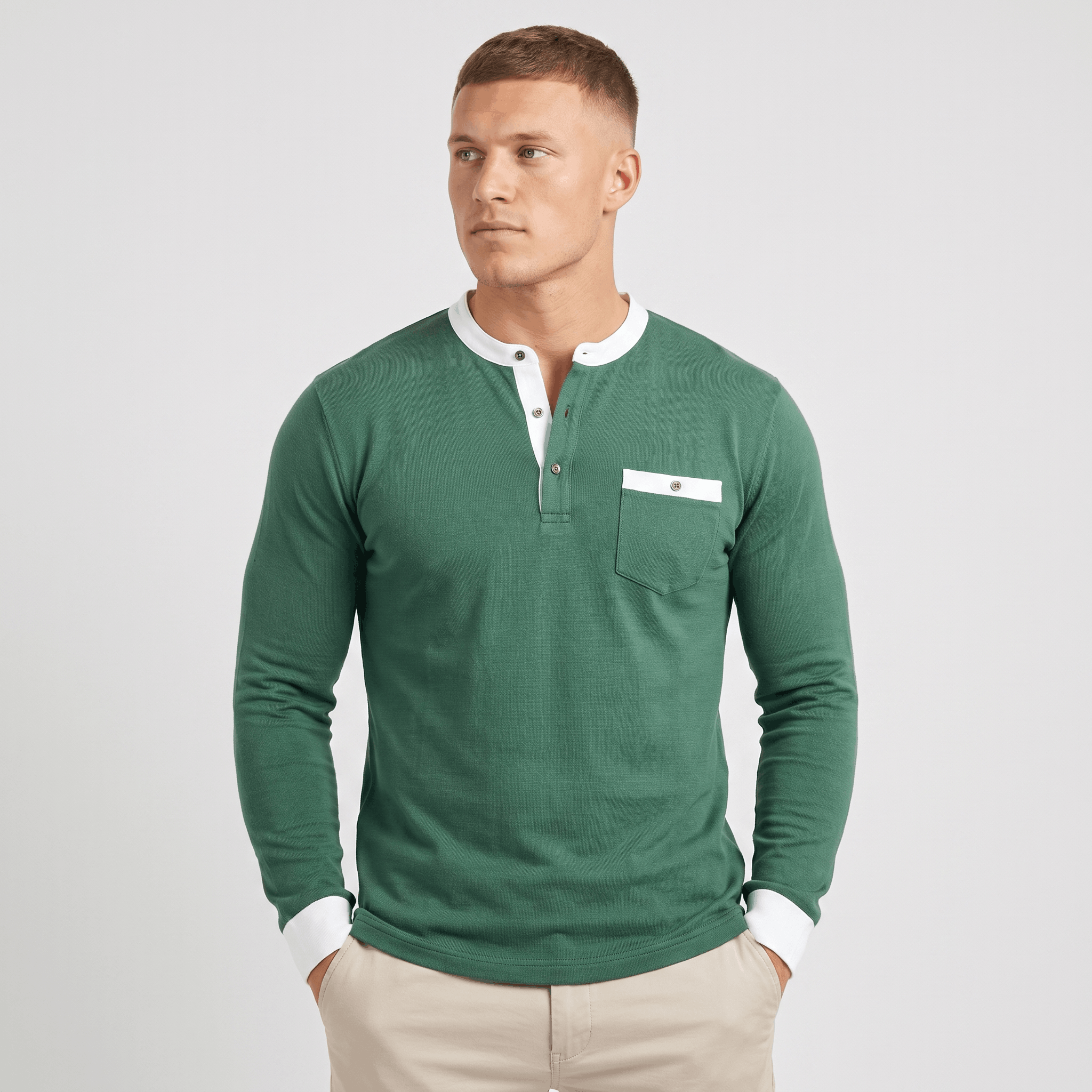 Man wearing a green long-sleeve Henley sweater with a white contrast placket, chest pocket detail, and modern slim fit.