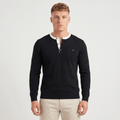 Man wearing a black long-sleeve Henley sweater with a white contrast placket and collar trim, three-button neckline, chest logo, and modern slim fit.