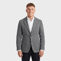 Man wearing a gray textured tweed blazer with a notched lapel, two-button closure, flap pockets, and tailored fit over a white dress shirt and black trousers.