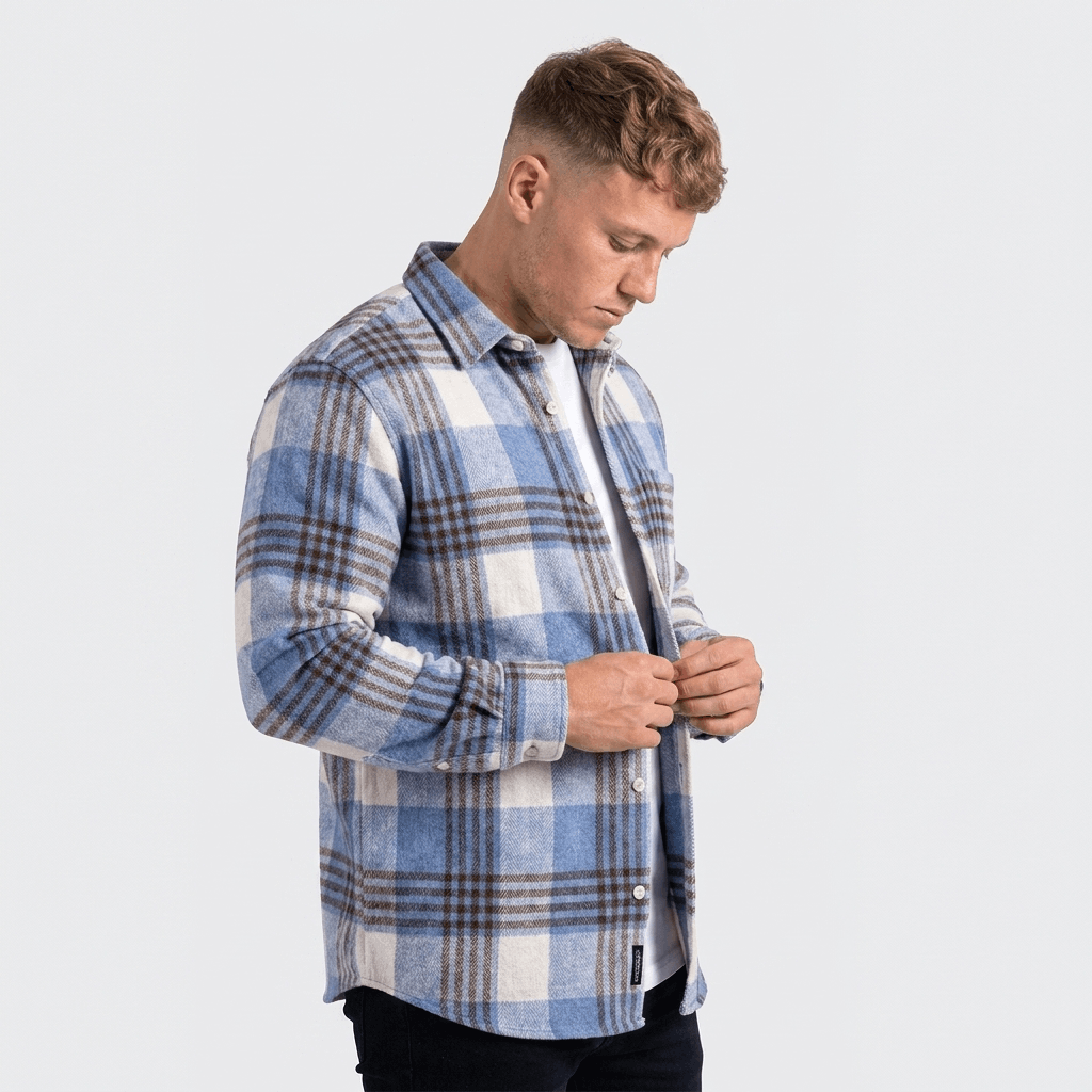 Side view of a man wearing a blue and white plaid overshirt jacket with a button-front closure and long sleeves.