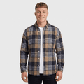 Man wearing a navy, beige, and white plaid overshirt jacket with a button-front closure, spread collar, chest pockets, and long sleeves over a white shirt and black trousers.