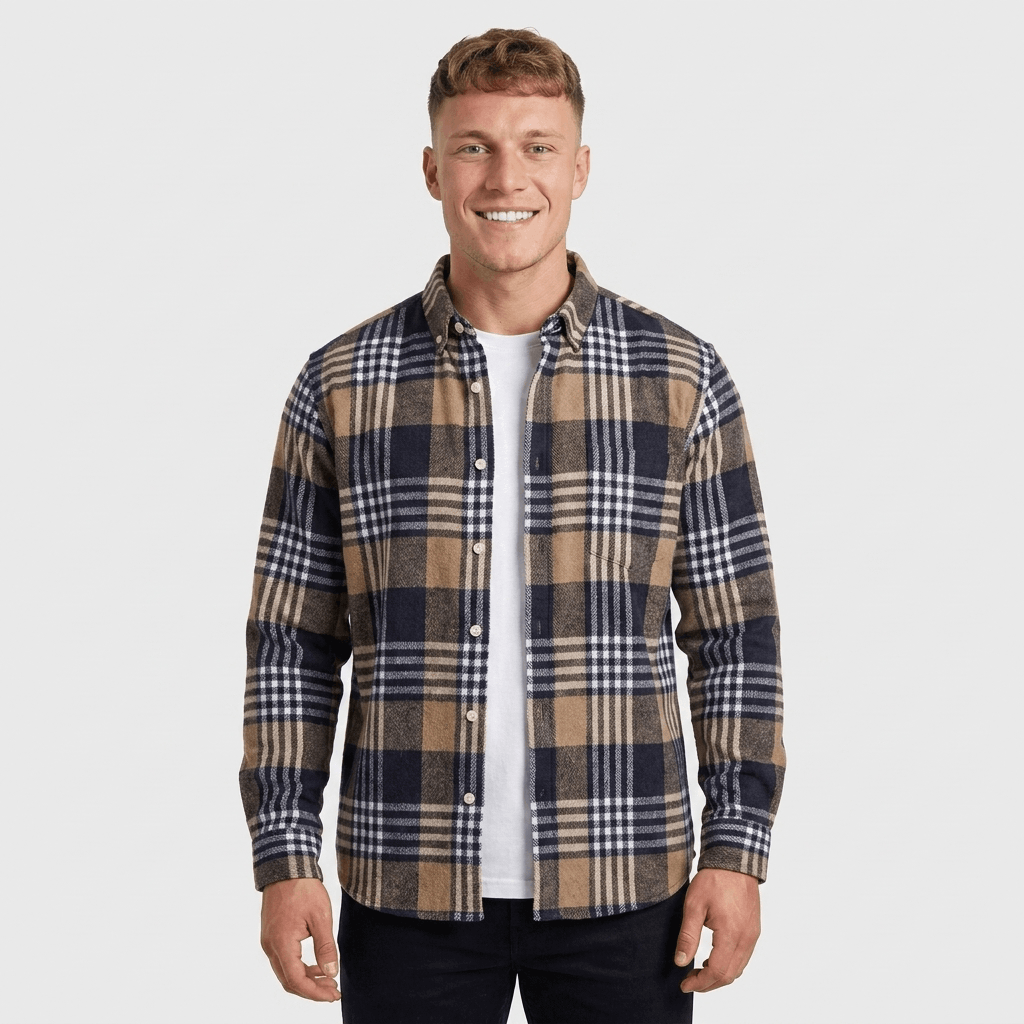 Man wearing a navy, beige, and white plaid overshirt jacket with a button-front closure, spread collar, chest pockets, and long sleeves over a white shirt and black trousers.