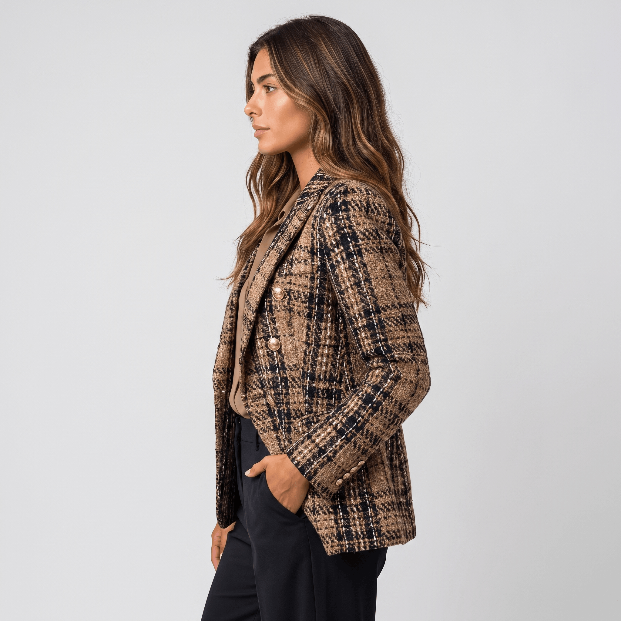 Side view of a woman wearing a brown plaid tweed blazer with a tailored fit, notched lapels, and long sleeves.