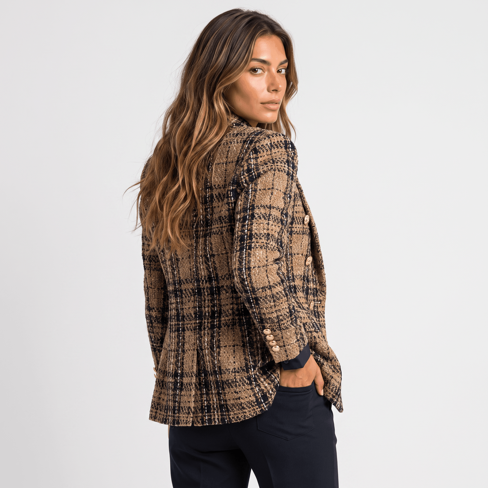 Side view of a woman wearing a brown plaid tweed blazer with a tailored fit, notched lapels, and long sleeves.