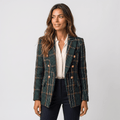 Woman wearing a dark green plaid tweed blazer with gold-tone buttons, notched lapels, flap pockets, and tailored silhouette over a white blouse and dark trousers.