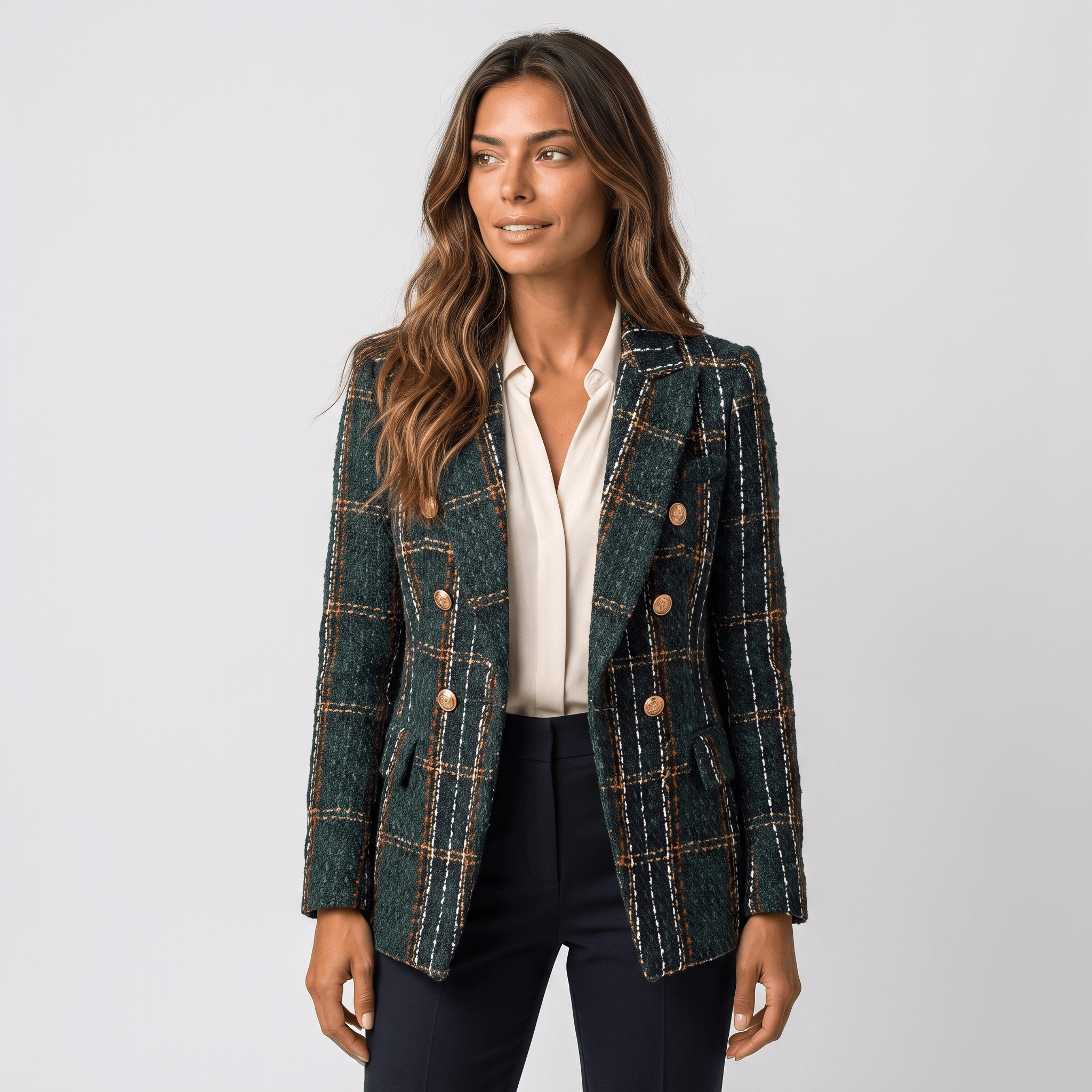 Woman wearing a dark green plaid tweed blazer with gold-tone buttons, notched lapels, flap pockets, and tailored silhouette over a white blouse and dark trousers.