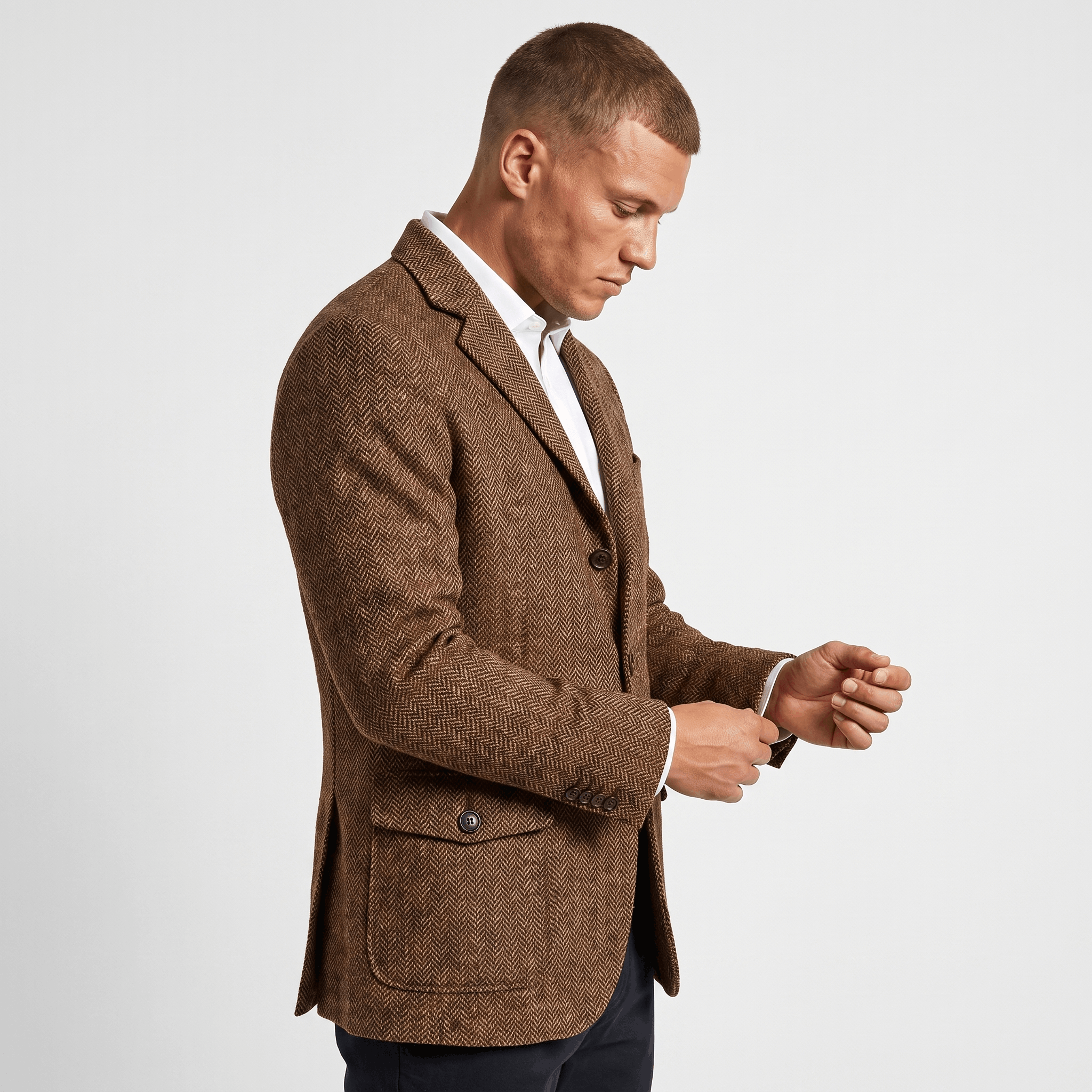 Side view of a man wearing a brown tweed blazer with a notched lapel, flap pockets, and tailored fit.