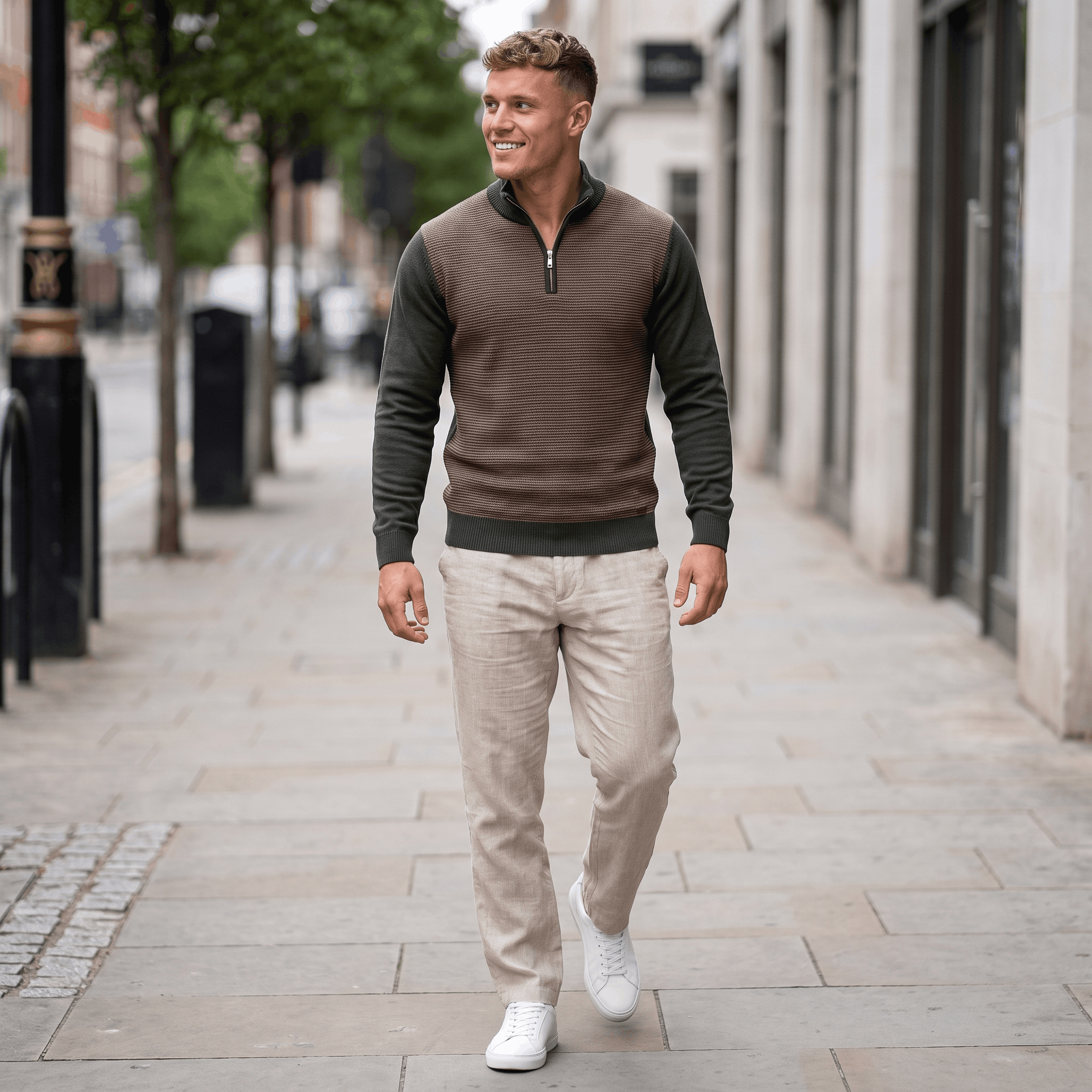 Man wearing a brown and olive green color block quarter-zip sweater with beige trousers walking outdoors.