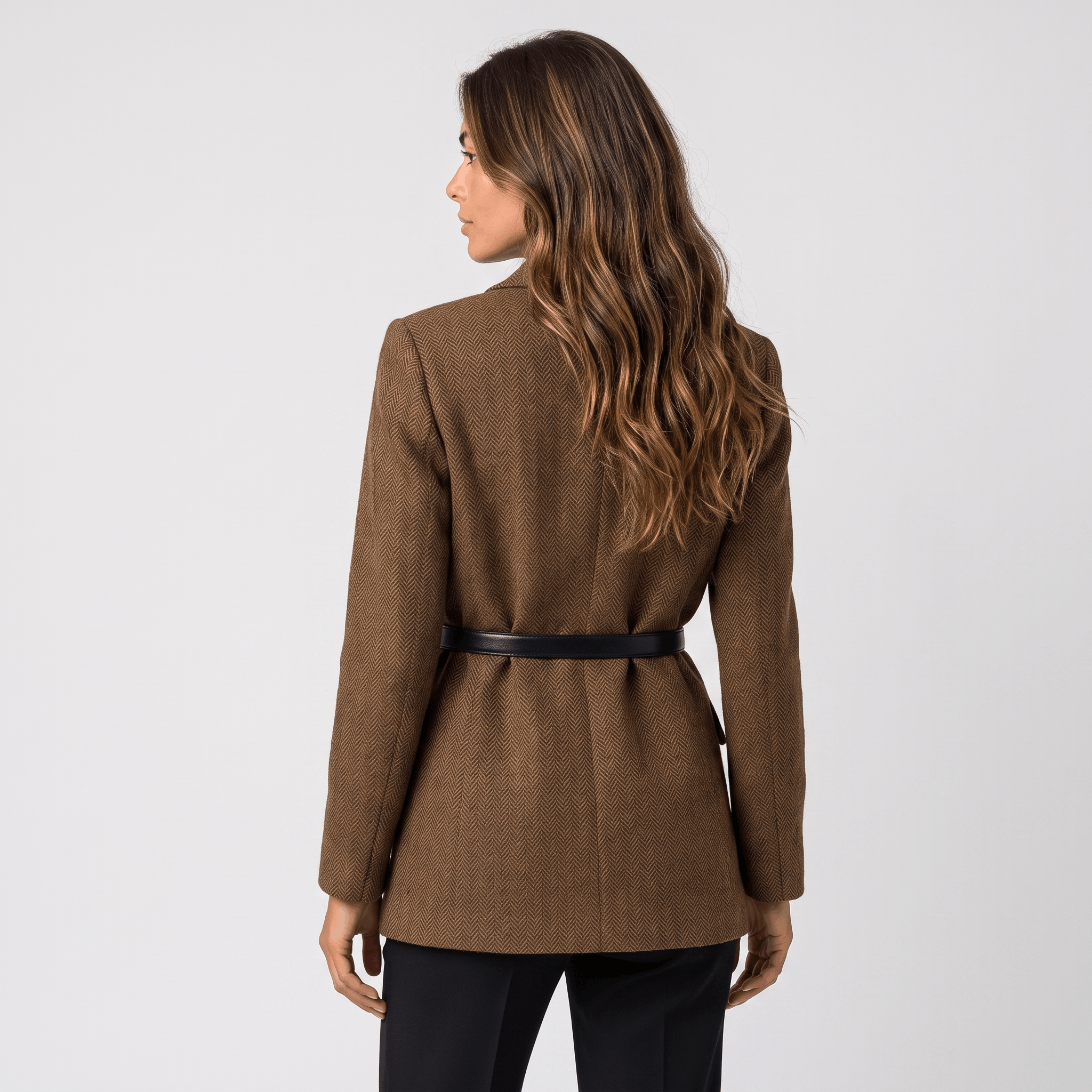 Back view of a woman wearing a brown tweed blazer with a belted waist, tailored silhouette, and long sleeves.