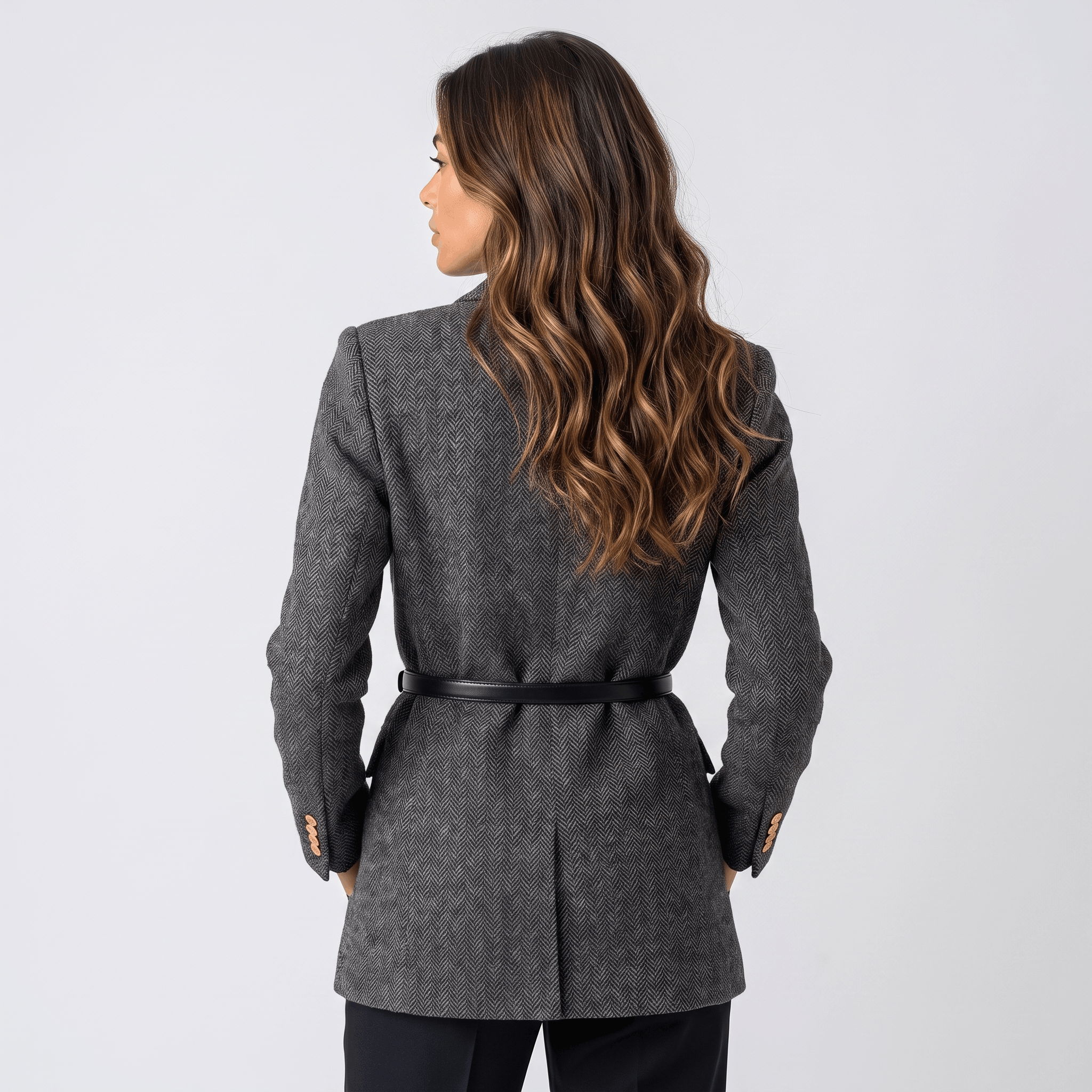 Back view of a woman wearing a charcoal gray tweed blazer with a belted waist and fitted tailored design.