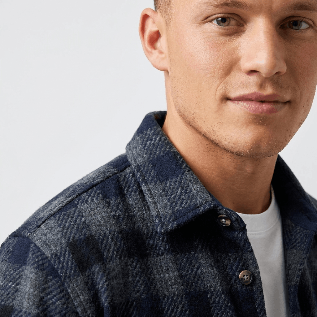 Close-up of a navy blue plaid overshirt jacket showing the textured plaid fabric, collar, and button-front detail.