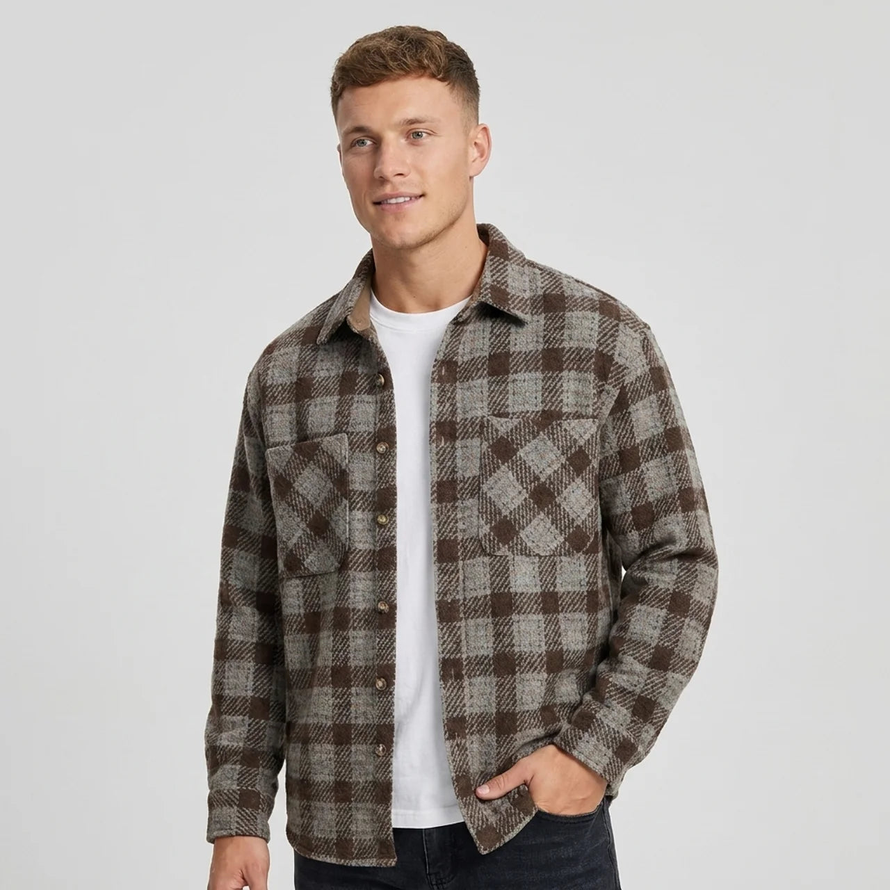 Man wearing a brown and gray plaid overshirt jacket with a button-front closure, pointed collar, chest pockets, and relaxed fit over a white shirt.